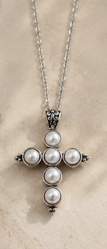 Cross-shaped necklace with pearl-like beads on a beige background