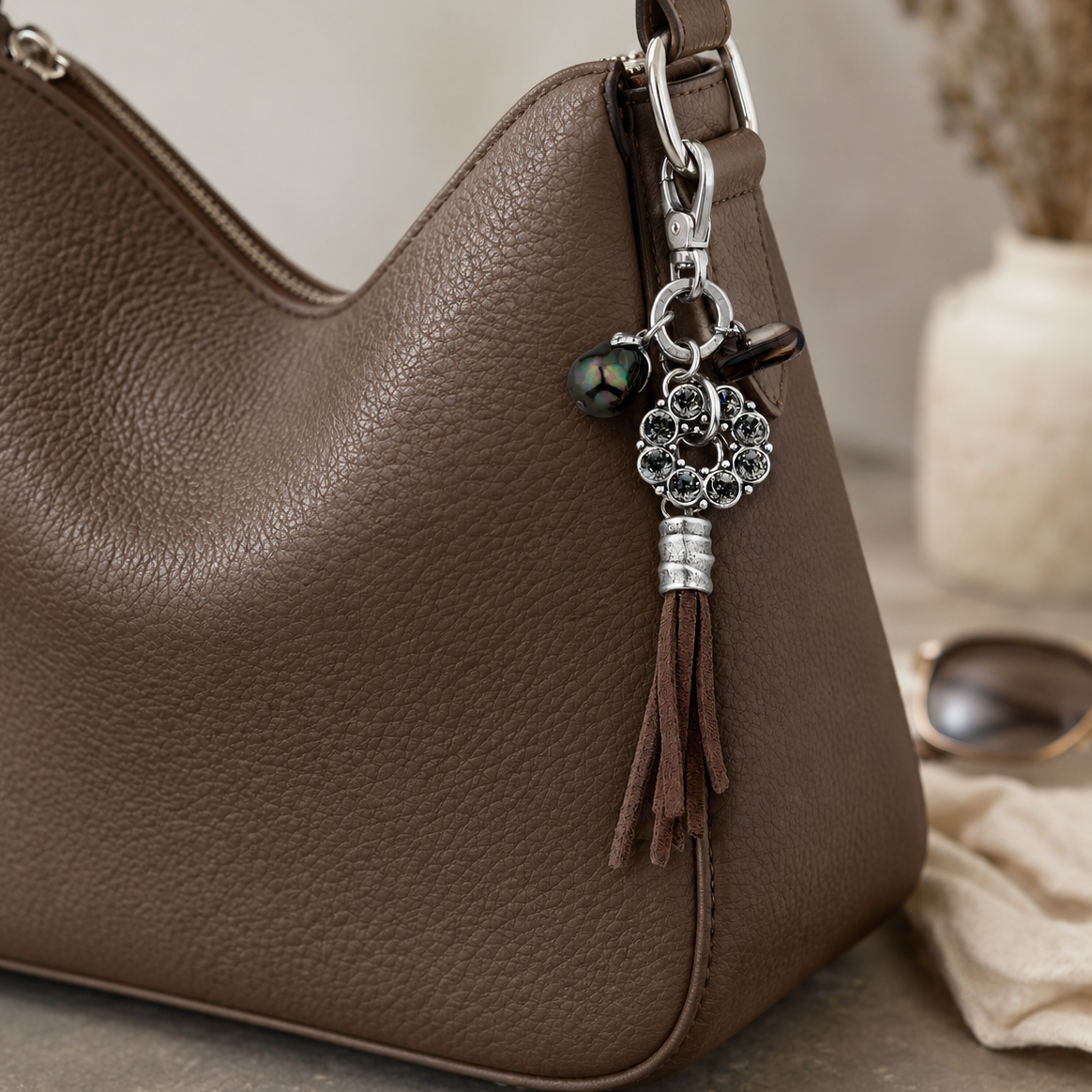 Brown leather handbag with a decorative keychain on a neutral background