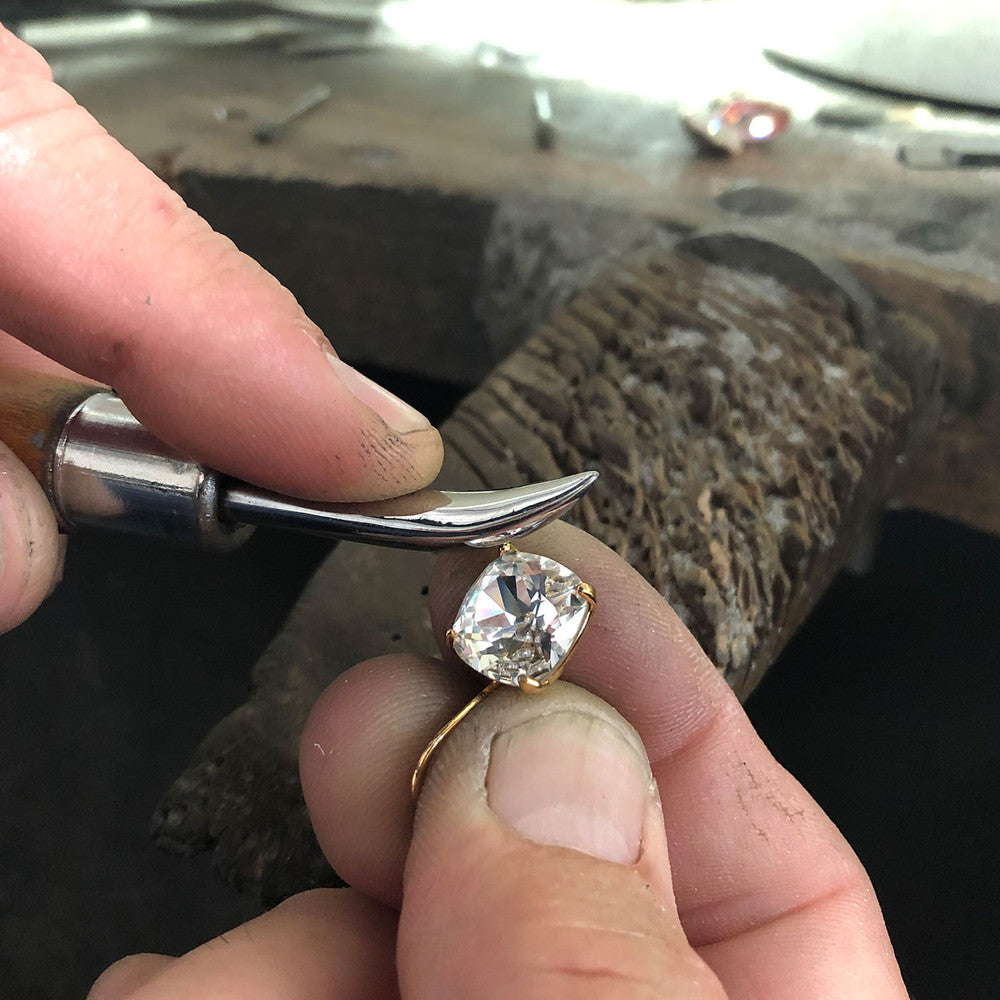 Close-up of a hand holding a Crystal Cushion Earring with a blurred background of a workshop.