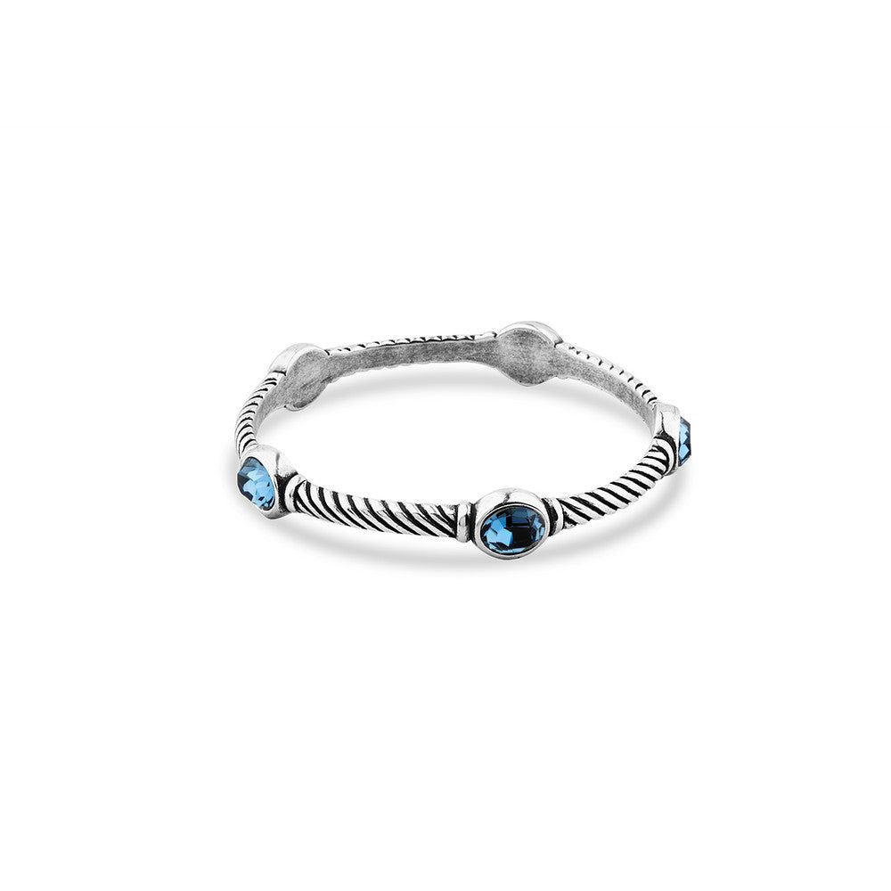 A silver-toned twisted bangle bracelet featuring five round-cut denim blue gemstones, displayed on a clean white background.
