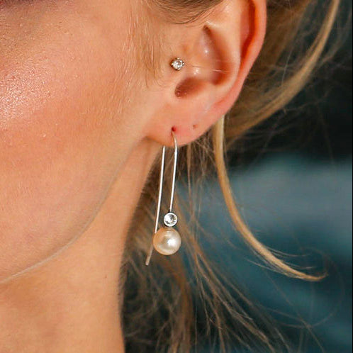 A close-up image of a woman's face, focusing on her wearing silver Starry Night Earring Threads with white pearls.