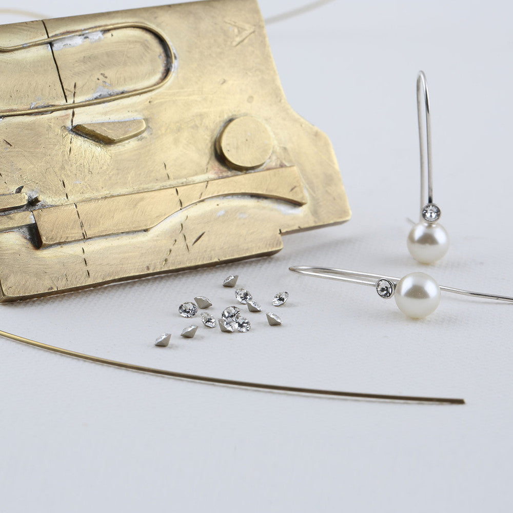 Gold sculpture, pearl earrings, and Swarovski crystals on a white background