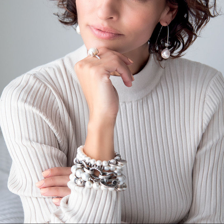 Woman wearing a white ribbed sweater with Miglio pearl bracelets, ring and earrings.
