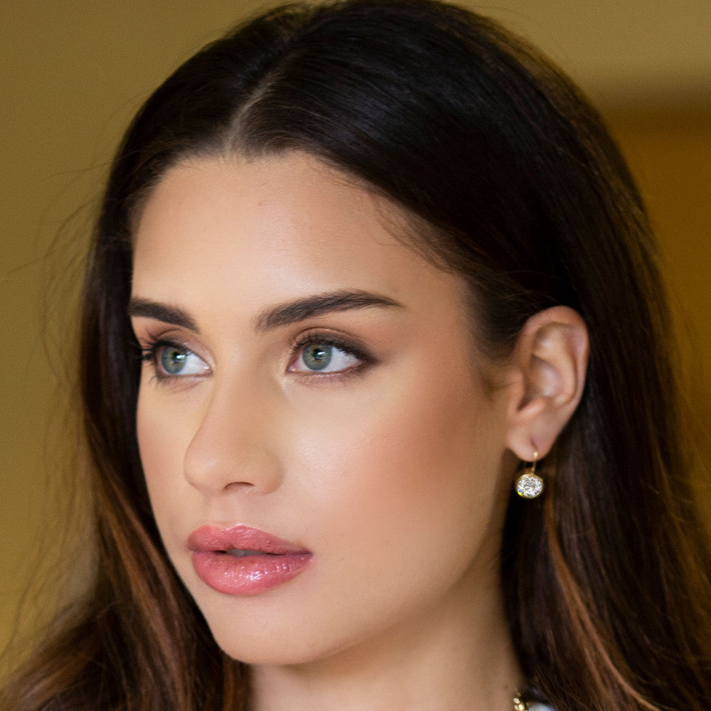 Close-up of a woman's face wearing 18ct Gold-plated Petite Glam Rock earrings with a neutral background.