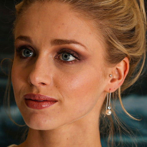 A close-up image of a woman's face, focusing on her wearing silver Starry Night Earring Threads with white pearls.