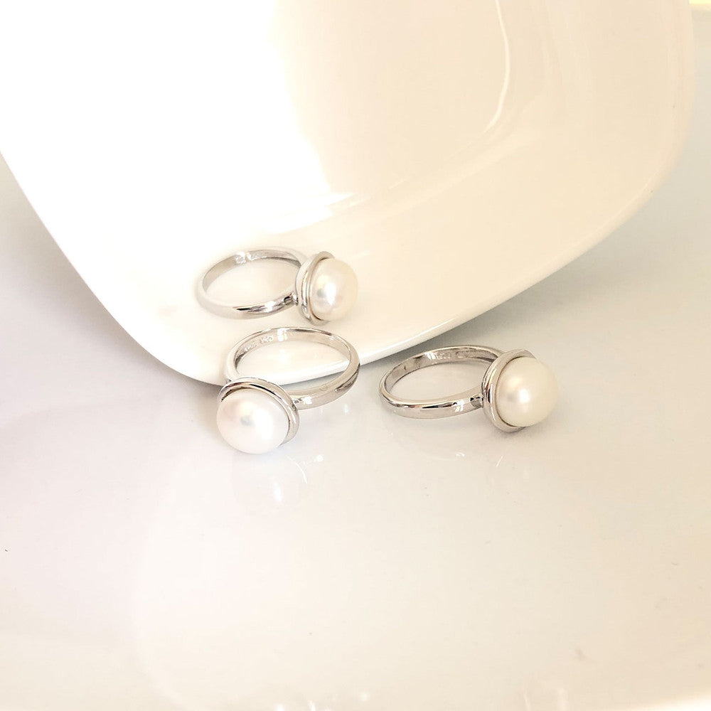 Three silver rings with pearls on a white ceramic plate.