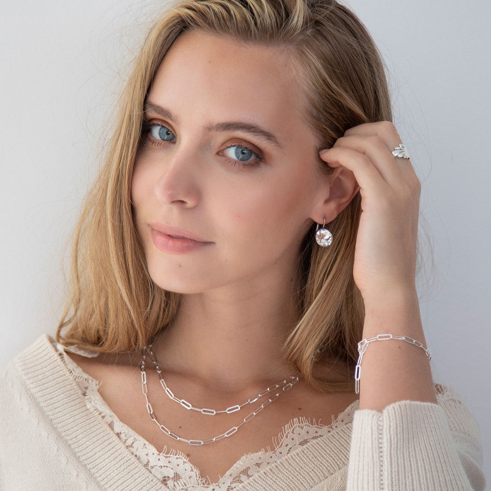 A person wearing a white top and showcasing a sterling silver paperclip bracelet on their wrist.