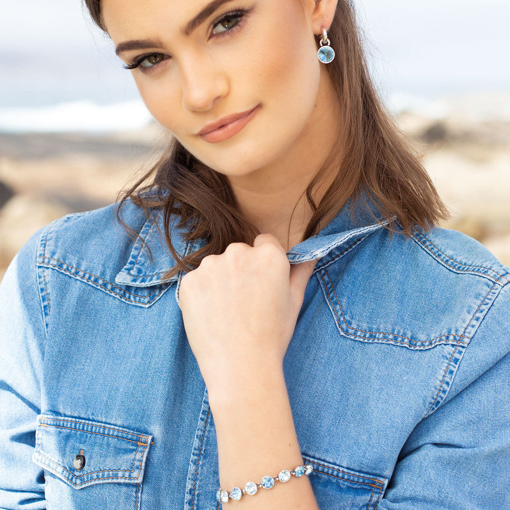 Woman wearing a blue denim jacket with Miglio Jewellery with a blurred outdoor background