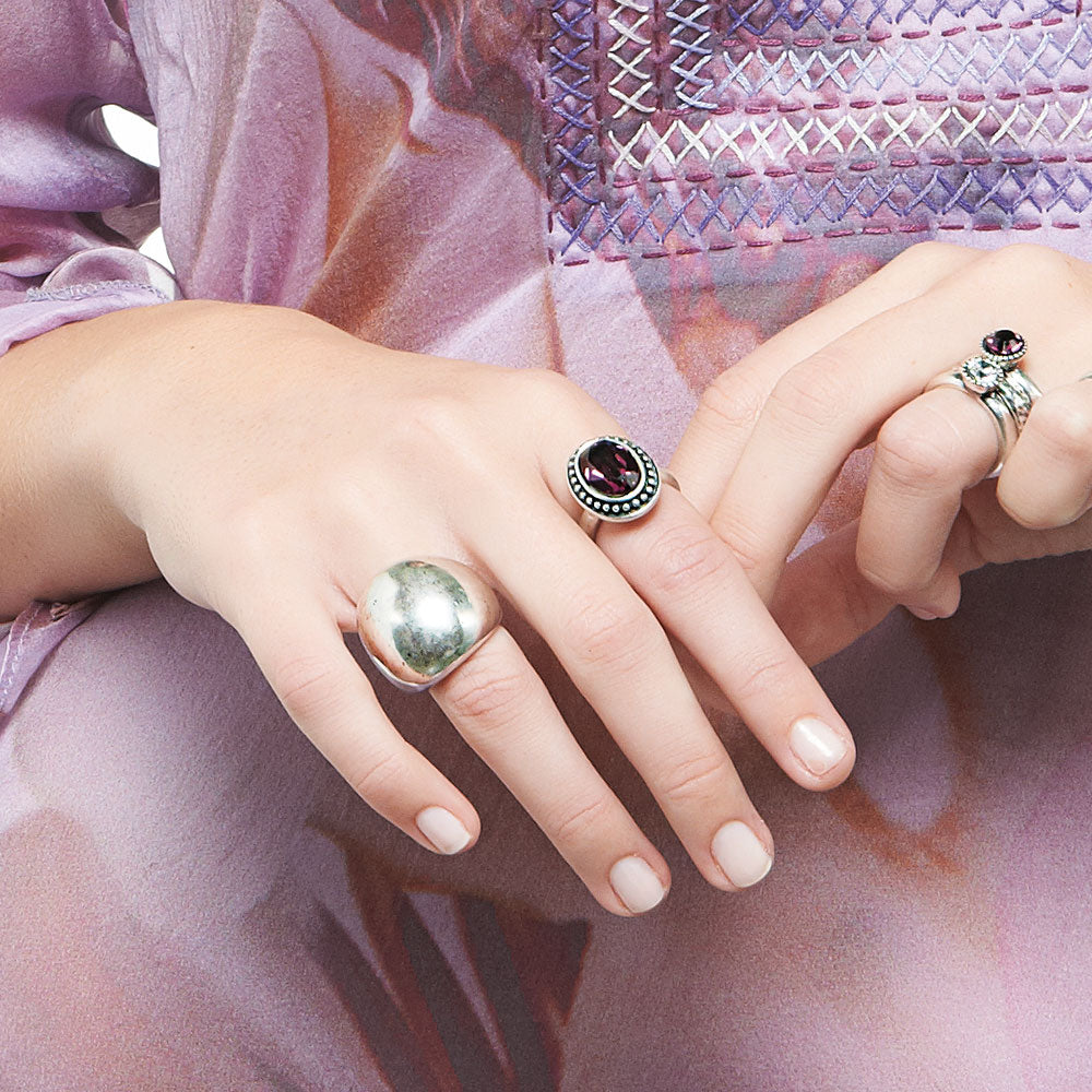 Close-up of hands wearing Miglio  silver rings with Swarovski gemstones on a pink textured background