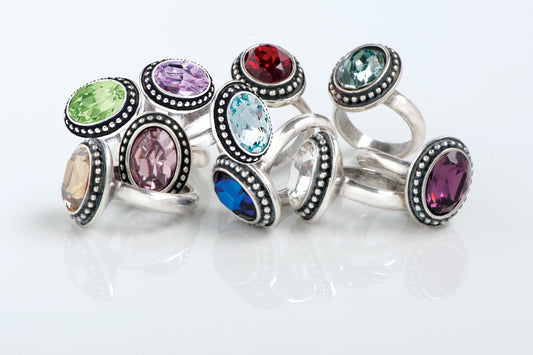 Set of silver 14mmx10mm Oval Swarovski rings with multicolored gemstones on a white background.