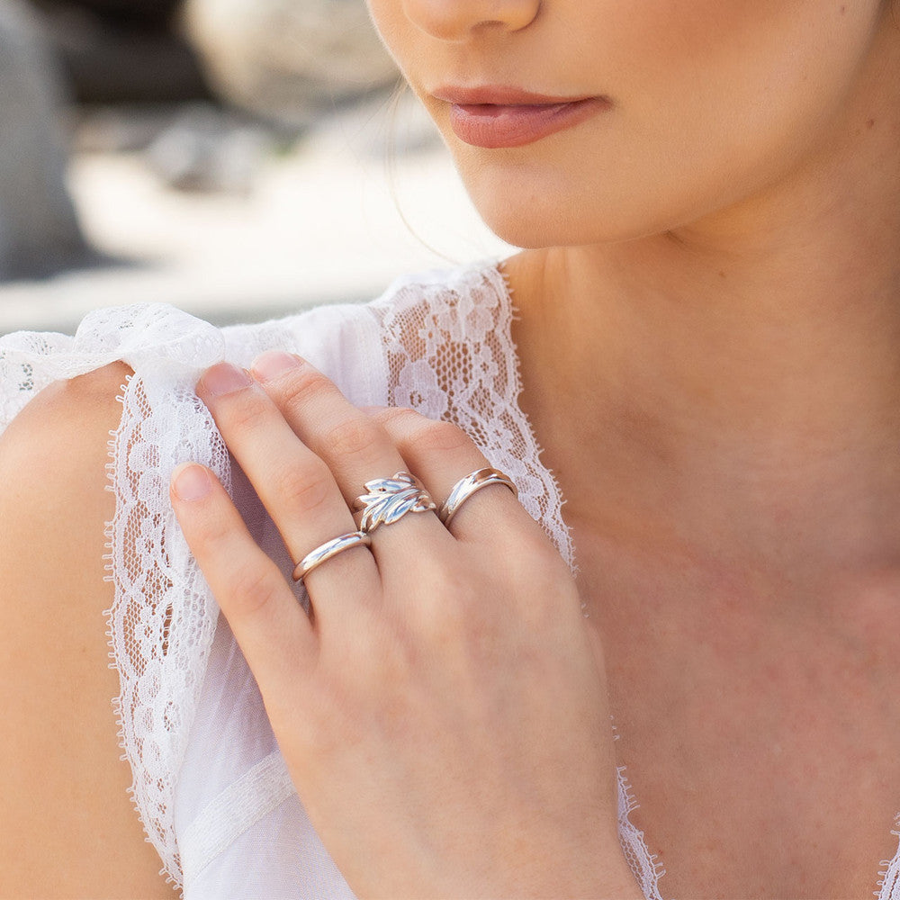 A close-up lifestyle shot of a woman wearing three silver ,Miglio rings on her fingers, set against a soft-focus outdoor background.